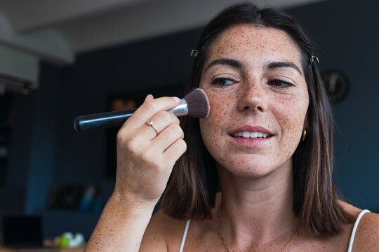 Woman with freckle face applying makeup at home