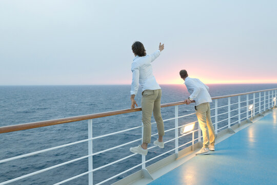 Young men standing on deck of ship, watching sunset