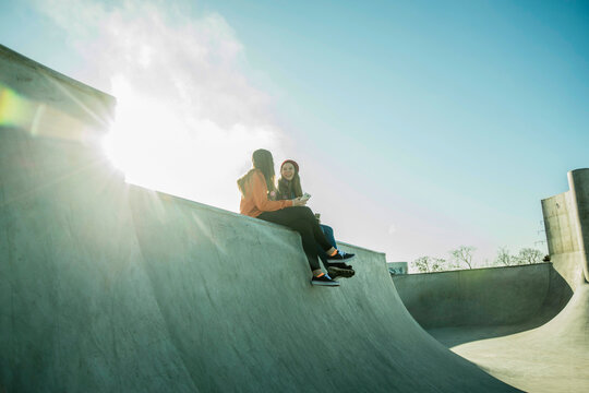 Two teenage girls in skatepark sharing cell phone