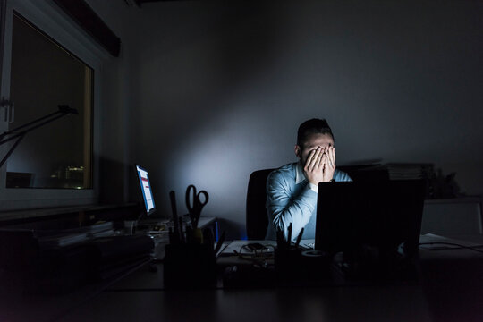 Exhausted businessman sitting at desk in office at night