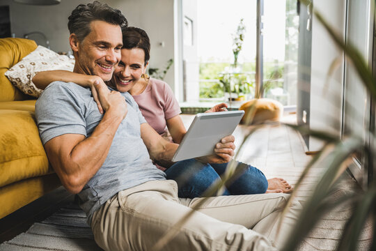 Smiling woman with arm around man looking at digital tablet while sitting at home