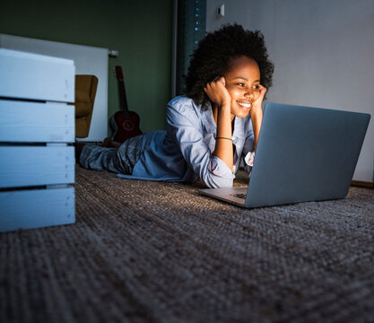Smiling woman lying on floor at home using laptop at night