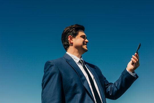 Businessman in suit checking smartphone outdoors against blue sky