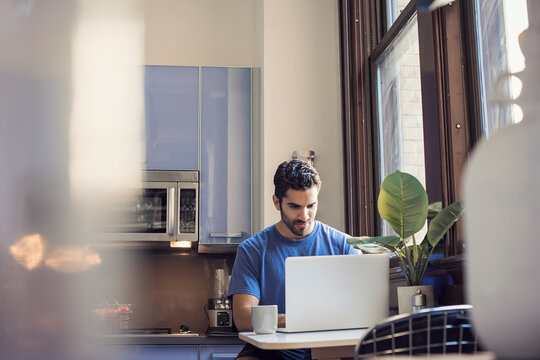Young man standing in kitchen using laptop