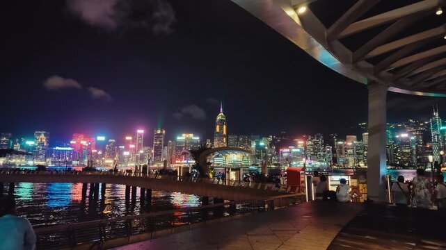 A dynamic nighttime scene of Hong Kong's skyline viewed through a pedestrian walkway or underpass