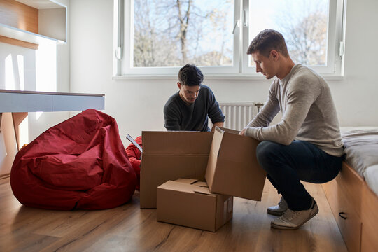 Two young men unpacking cardboard boxes in a room
