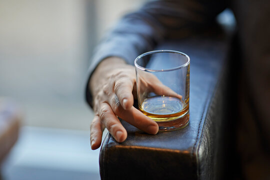 Close-up of man with whiskey glass on arm rest of a leather chair