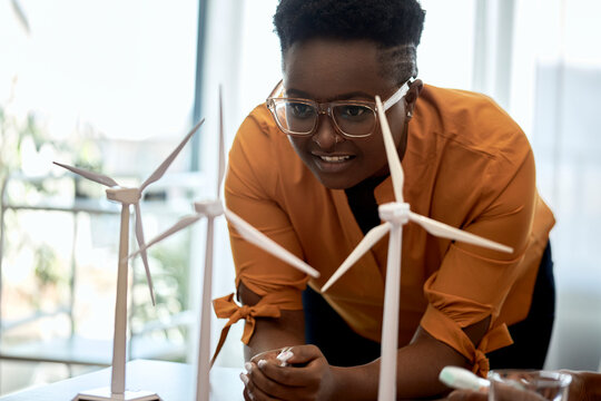 Woman wearing eyeglasses examining wind turbine models at office