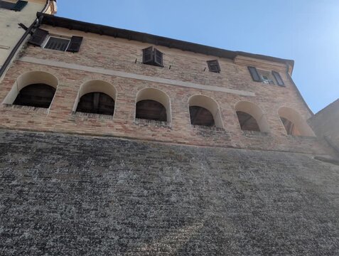 Edificio storico in mattoni a Morro d&rsquo;Alba, con archi al piano inferiore , poggiato su una parete in pietra inclinata. Cielo azzurro e atmosfera tipica dei borghi marchigiani
