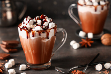 Fototapeta premium Glass cup of hot cocoa drink with whipped cream, marshmallows and liquid chocolate on dark background
