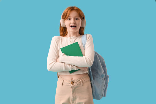 Teenage redhead girl with notebook and backpack on blue background