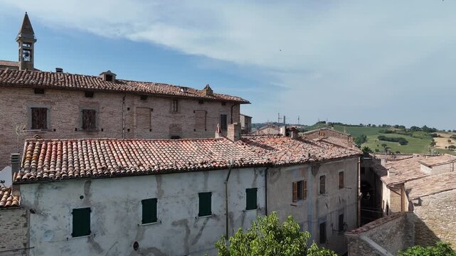 Veduta di San Vito sul Cesano con strada panoramica accanto a muro in pietra, edifici storici in pietra chiara e colline marchigiane sullo sfondo
