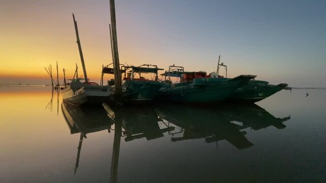 Beautiful sunset over the sea with traditional fishing boats floating on calm water, warm golden sky reflection.