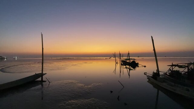 Beautiful sunset over the sea with traditional fishing boats floating on calm water, warm golden sky reflection.
