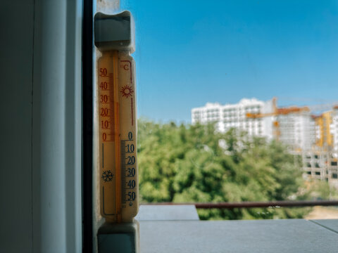Outdoor thermometer shows warm summer day near city construction site
