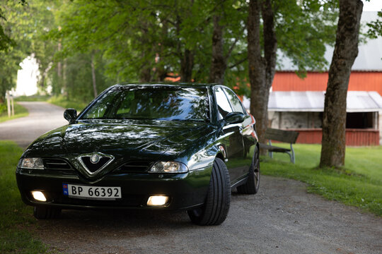 Dark green Alfa Romeo 166 sedan parked on gravel path beside trees