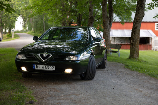 Dark green Alfa Romeo 166 sedan rests on gravel path beside trees
