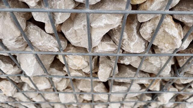 Close-up of pale limestone rocks inside a galvanized steel gabion cage, showing rough stone texture and wire grid construction detail.