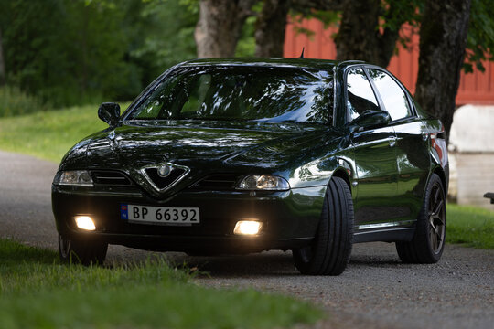 Dark green Alfa Romeo 166 sedan glows softly under twilight sky