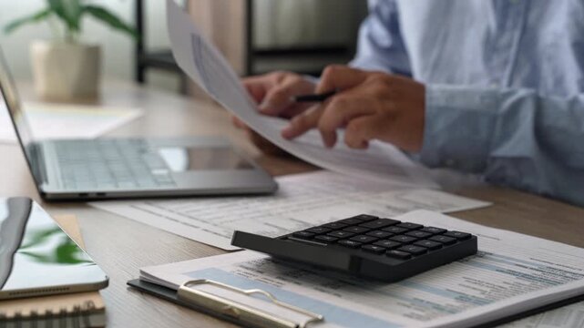 man use calculator while holding a financial document beside a laptop, showing budgeting, accounting, and report review workflow for corporate finance planning process.