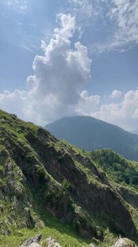Vertical nature footage captured at Malsa, Abbottabad, Pakistan, showcasing rugged mountain cliffs, lush green hills, dramatic white clouds, and a breathtaking blue sky. Ideal for travel videos, 