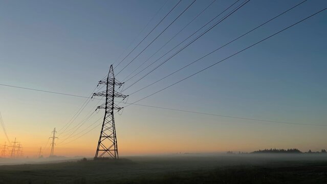 High voltage power transmission lines at sunrise with morning fog, electricity pylons across rural landscape, energy infrastructure, scenic industrial background