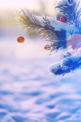 Fototapeta premium Red Christmas bell hangs on a snow-covered branch of a Christmas tree against a festive background of white snow. Christmas tree with decoration under snow