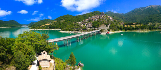 Castel di Tora Turano Lake Italy 8K Drone panorama. Diagonal bridge on stilts over turquoise water to hilltop medieval borgo town with church. Borghi piu belli d Italia most beautiful villages © Freesurf