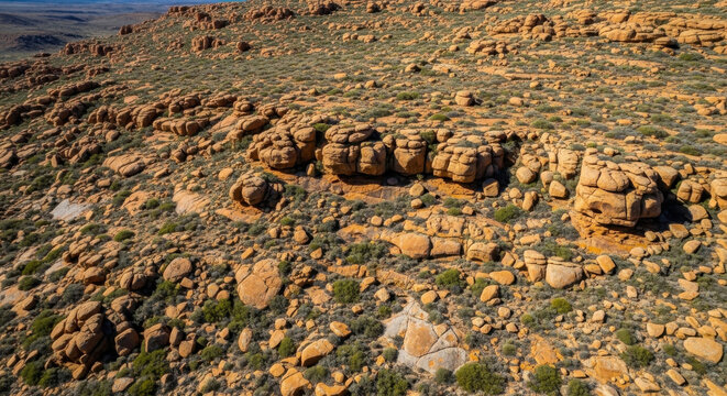 Aerial view of rugged orange rock formations and ancient boulders in a remote desert landscape wilderness.