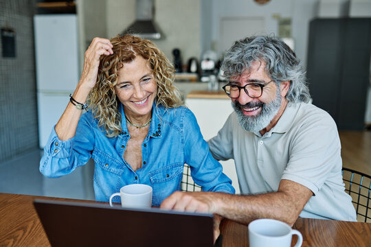 Portrait of a lovely senior mature couple using a laptop together and having fun drinking coffee or tea sitting at a table at home
