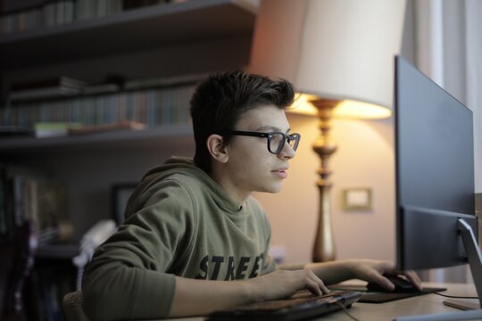 Teenage boy with glasses focused on desktop computer
