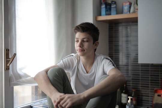Pensive teenage boy sitting alone by a window