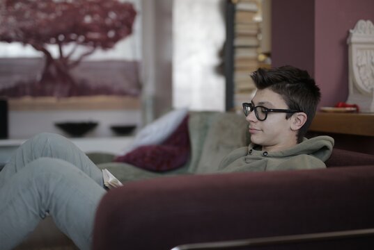 Young man with glasses reading a book at home