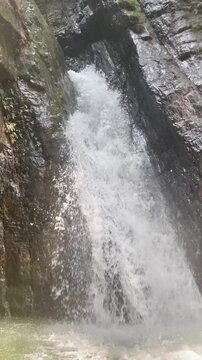 A beautiful vertical video of a crystal-clear waterfall flowing between rugged rock formations in a peaceful natural setting, this footage ideal for travel, adventure, relaxation, wellness, meditation