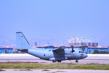 Fototapeta premium Military transport plane taking off on a runway with city buildings behind