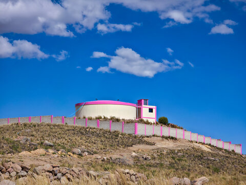 Cream and pink water tank atop a hill with concrete perimeter fence