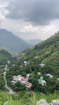 A breathtaking vertical view of the lush green mountain valley in Malsa, Abbottabad, Pakistan. Featuring winding roads, village homes, forested hills, and dramatic cloudy skies