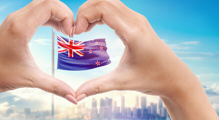 New Zealand national flag. Two hands forming a heart shape in front of a national flag waving in beautiful clouds. New Zealand national flag behind the heart shape hand.
