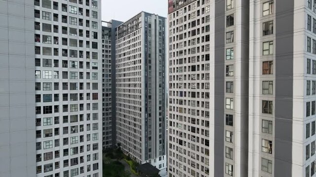 Aerial drone footage descending along the facade of modern high-rise apartment towers, revealing a large swimming pool in the residential complex