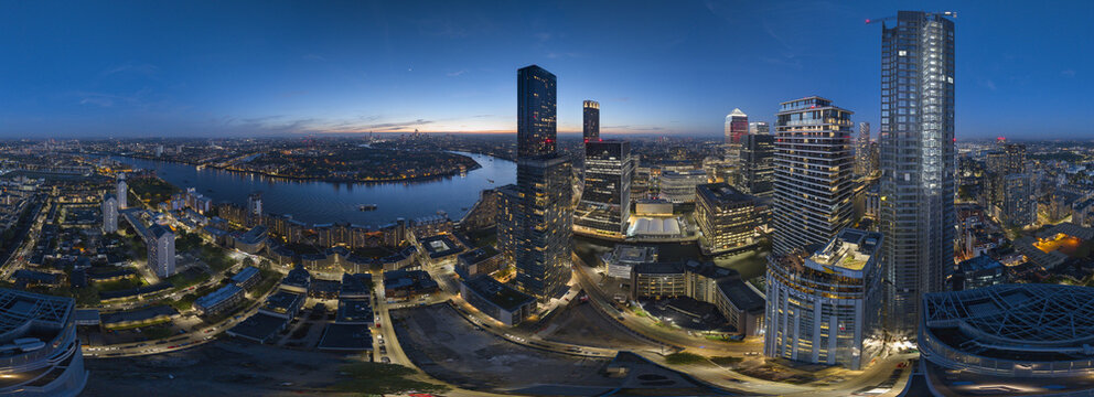 Aerial view of Canary Wharf Estate at dusk with illuminated skyscrapers, the River Thames winding through the city, and urban infrastructure in London, England, United Kingdom.