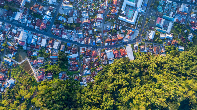 Aerial view of the town of Bajawa with its dense residential rooftops, winding roads, and lush green forest borders in Bajawa, Nusa Tenggara Timur, Indonesia.