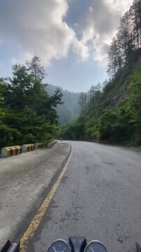 Bike ride on the scenic Government House track in Murree, Pakistan. Front view with speedometer, yellow-lined road, white wooden fence, and tall trees along the peaceful path in pleasant weather.