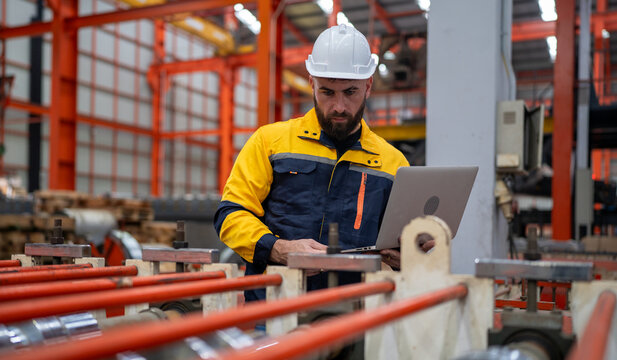 Industrial engineer in safety helmet uniform jacket working in heavy steel engineering factory. Technician manager worker inspector using laptop in metalwork product manufacturing facility workplace