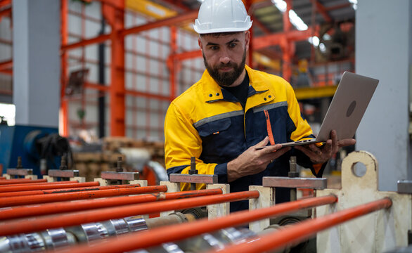 Industrial engineer in safety helmet uniform jacket working in heavy steel engineering factory. Technician manager worker inspector using laptop in metalwork product manufacturing facility workplace