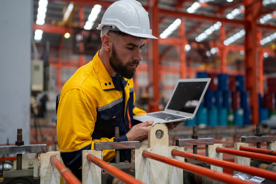 Industrial engineer in safety helmet uniform jacket working in heavy steel engineering factory. Technician manager worker inspector using laptop in metalwork product manufacturing facility workplace