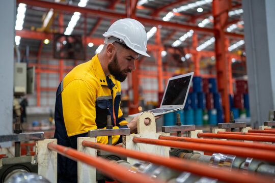 Industrial engineer in safety helmet uniform jacket working in heavy steel engineering factory. Technician manager worker inspector using laptop in metalwork product manufacturing facility workplace
