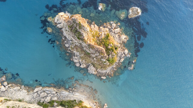 Aerial view of the rocky outcrop at Paralia Fieroulas surrounded by clear turquoise waters and rugged coastline in Greece.
