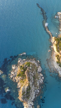 Aerial view of the rocky islet at Paralia Fieroulas surrounded by clear turquoise waters and rugged coastline in Greece.