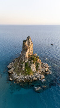 Aerial view of Paralia Fieroulas, a prominent rocky sea stack rising from the clear blue waters of the Ionian Sea, featuring rugged cliffs and sparse vegetation in Greece.
