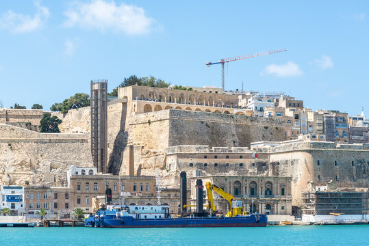 Valletta waterfront in Malta shows historic bastions and modern infrastructure, with the Upper Barrakka Gardens centred above the Grand Harbour and the Barrakka Lift tower rising beside the stone fort